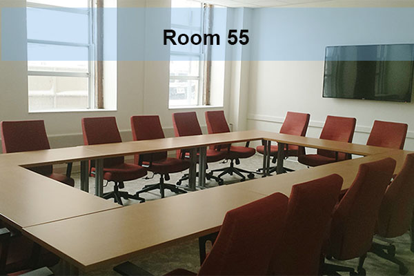 A conference room with tables, chairs, and a wall mounted monitor